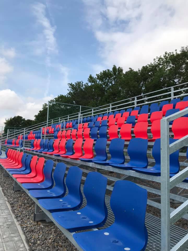 Nová tribuna se střídajícími červenými a modrými sedadly na fotbalovém stadionu v Poděbradech.